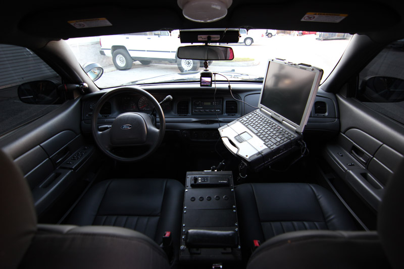 2004 Ford Crown Victoria interior showing dashboard, steering wheel, laptop mounted on console, and black leather seats