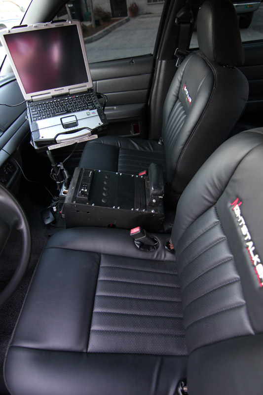 2004 Ford Crown Victoria police car interior showing laptop mounted on dash and equipment console between seats