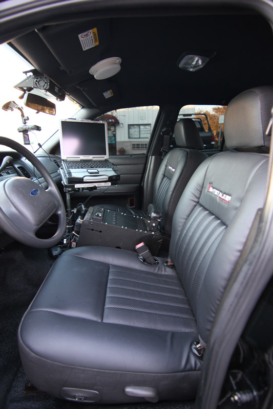 Interior of a police car showing front seats, laptop, and console