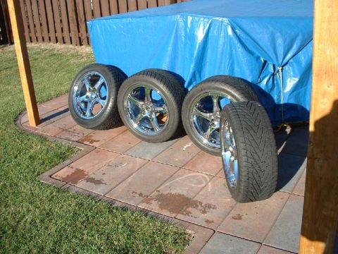 2000 Ford Crown Victoria - Four chrome wheels and tires are displayed on a paved patio area.