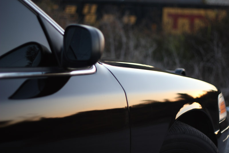 Close-up of black sedan's fender and side mirror with sunset reflection
