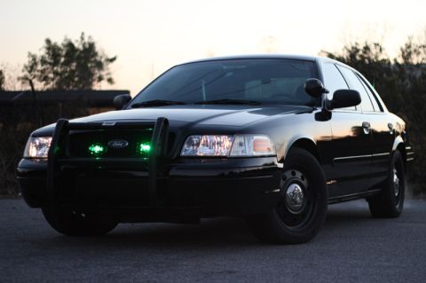 2004 Ford Crown Victoria - A black 2004 Ford Crown Victoria sits parked on a road with a push bar and green lights.