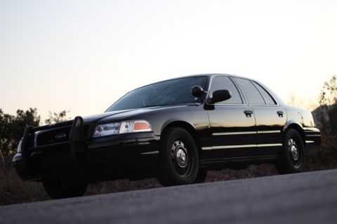 2004 Ford Crown Victoria - Black 2004 Ford Crown Victoria police car with push bumper, parked on the side of a road.