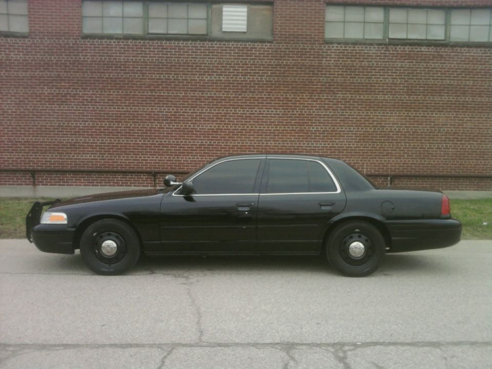 Side view of a black 2004 Ford Crown Victoria police car parked on asphalt in front of a brick building