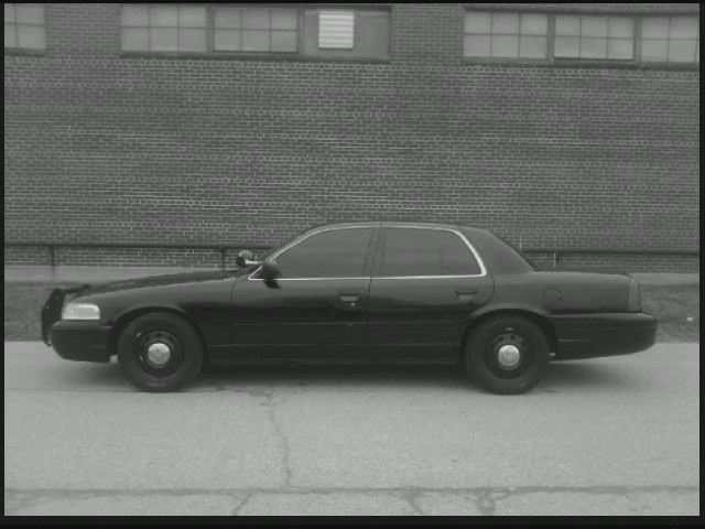 Black 2004 Ford Crown Victoria police car, side view, parked on pavement in front of brick building