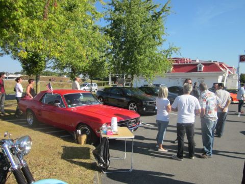 1991 Ford LTD Crown Victoria - A red 1967 Ford Mustang coupe is displayed at an outdoor event, with several other vehicles and people in the background.