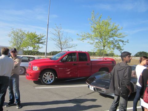 1991 Ford LTD Crown Victoria - A red pickup truck is parked in a lot with other vehicles and people around.