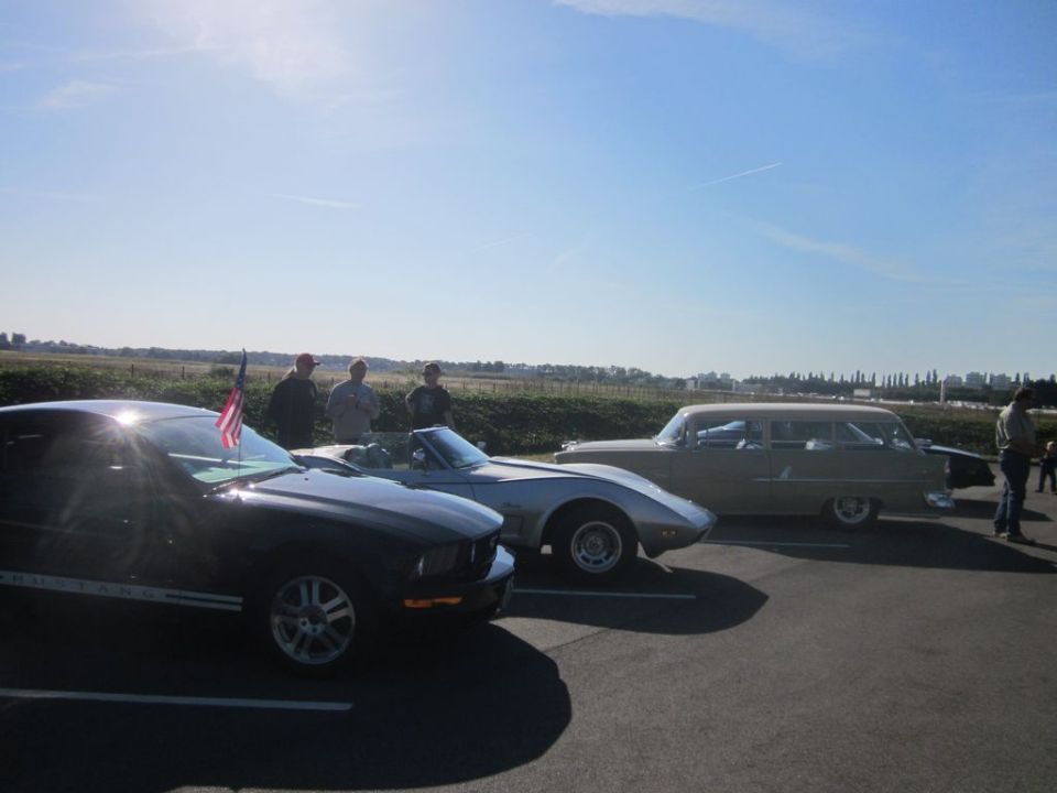Three cars parked side-by-side: a black modern Mustang, a silver convertible, and a tan station wagon