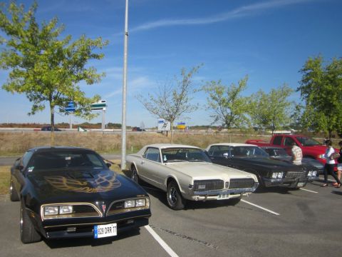 1991 Ford LTD Crown Victoria - A black 1977 Pontiac Firebird Trans Am is parked in a lot with other classic cars under a clear blue sky.
