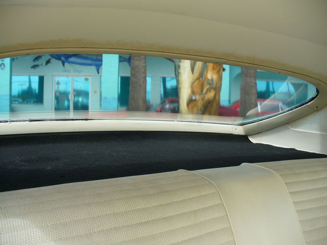 Interior rear window view of a car, showing a building with a mural and palm trees outside. Watermark reads SUPERMOTORS