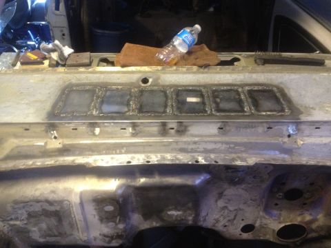 1965 Ford Mustang - A metal panel with multiple square cutouts shows signs of recent welding, with a water bottle and cloth resting on its surface.