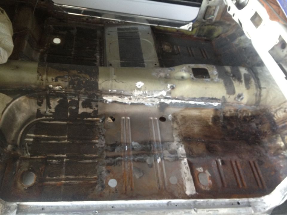 Car interior floor pan showing rust and repair work, viewed from above