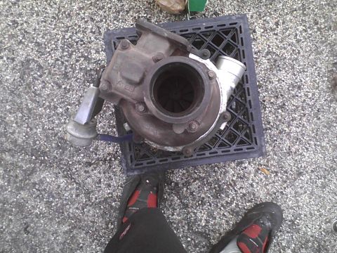 2003 Ford Crown Victoria - A turbocharger sits on a black grate, with a person's feet visible in the foreground.