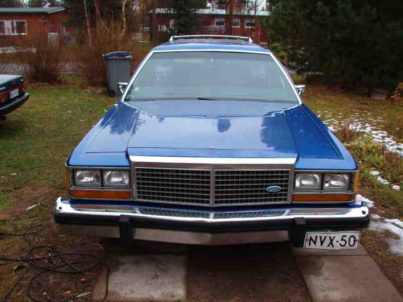 Front of a blue Ford wagon with chrome grille and NVX-50 plate parked outdoors.