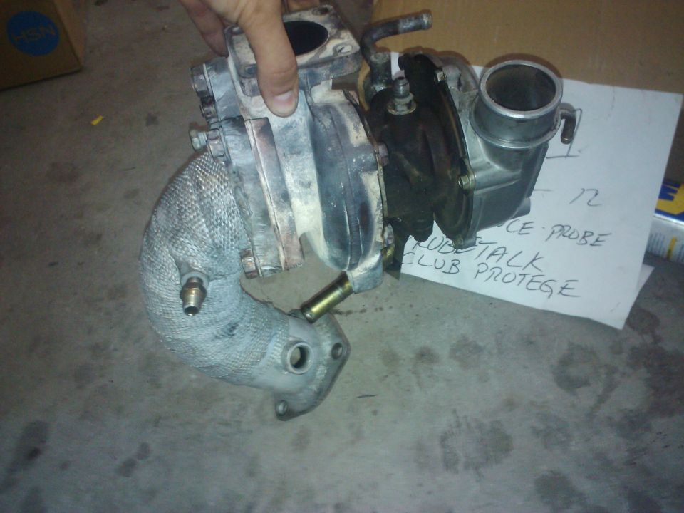 Turbocharger with heat wrap on exhaust manifold. Paper behind it says 'PROBE TALK CLUB PROTEGE'