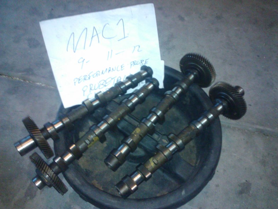 Four camshafts with gears in a black tray, paper with writing on the left