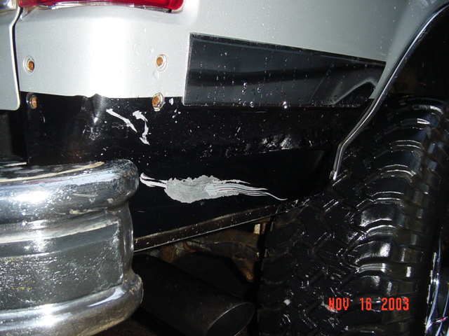 Close-up of rear bumper and quarter panel with white scuff marks and chrome wheel, dated Nov 16 2003