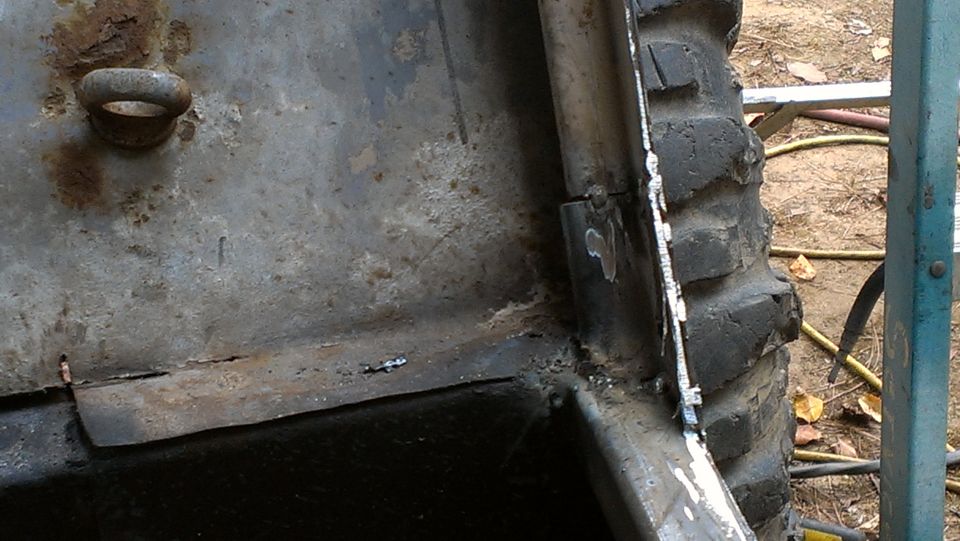 Rusted metal panel with tow hook, part of a tire, and welding marks