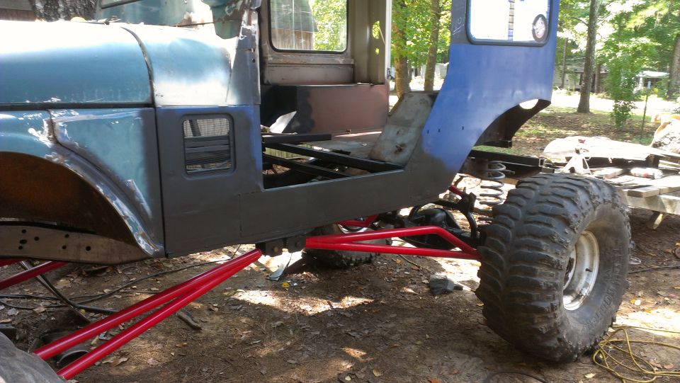 Blue and grey off-road vehicle chassis with red suspension components and large tires, undergoing modification