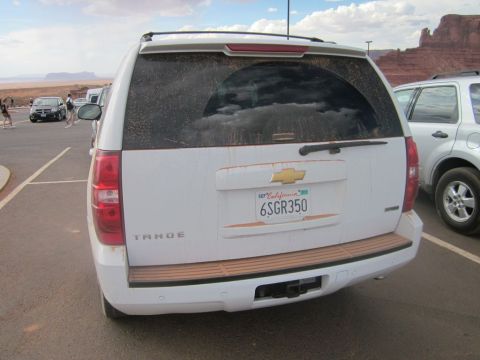 1991 Ford LTD Crown Victoria - A dusty white Chevrolet Tahoe SUV is parked in a lot with other vehicles and desert scenery.