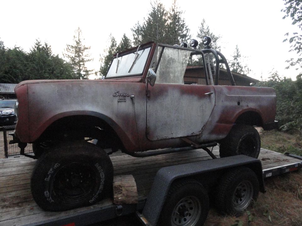 Red and white 1961 International Scout on a trailer, showing rust and missing parts