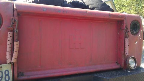 1961 International Scout 80 - Close-up of a red truck's tailgate, showing the International Harvester logo embossed in the center.