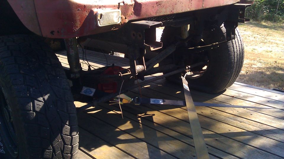 Rear axle, suspension, and tires of a red vehicle strapped to a wooden trailer