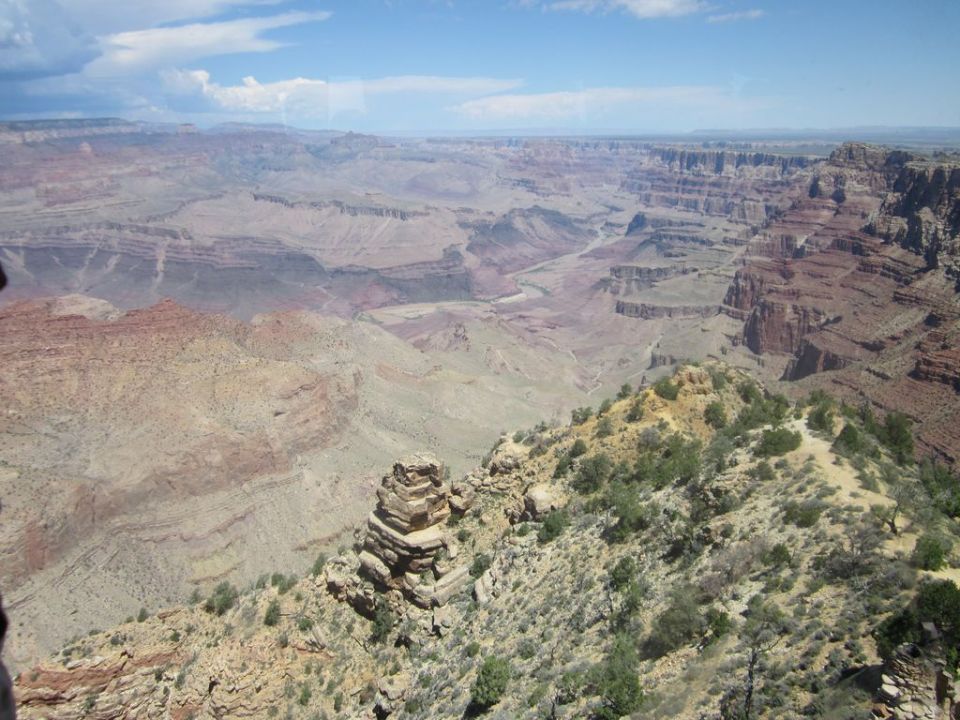 View of the Grand Canyon with layered rock formations and a blue sky with clouds. A website URL is visible in the lower right corner