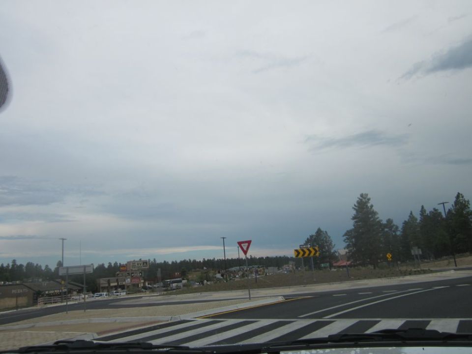Road intersection with yield and curve signs, buildings in background under cloudy sky