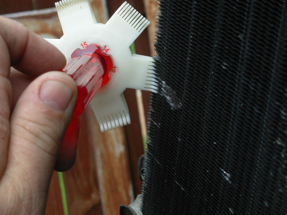 Hand using white fin comb tool to straighten black radiator cooling fins