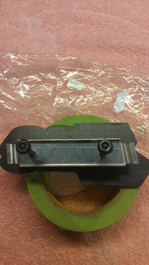1973 Chevrolet Camaro - A black automotive emblem is secured with screws to a metal bracket, placed on green painter's tape.