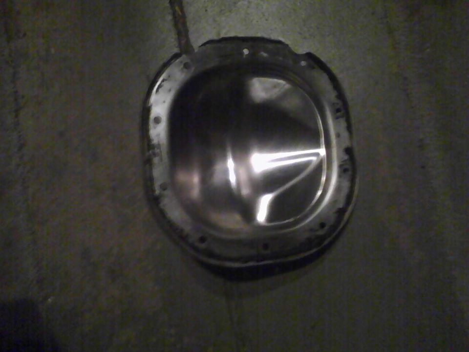 Differential cover with bolt holes around the perimeter, resting on a concrete surface