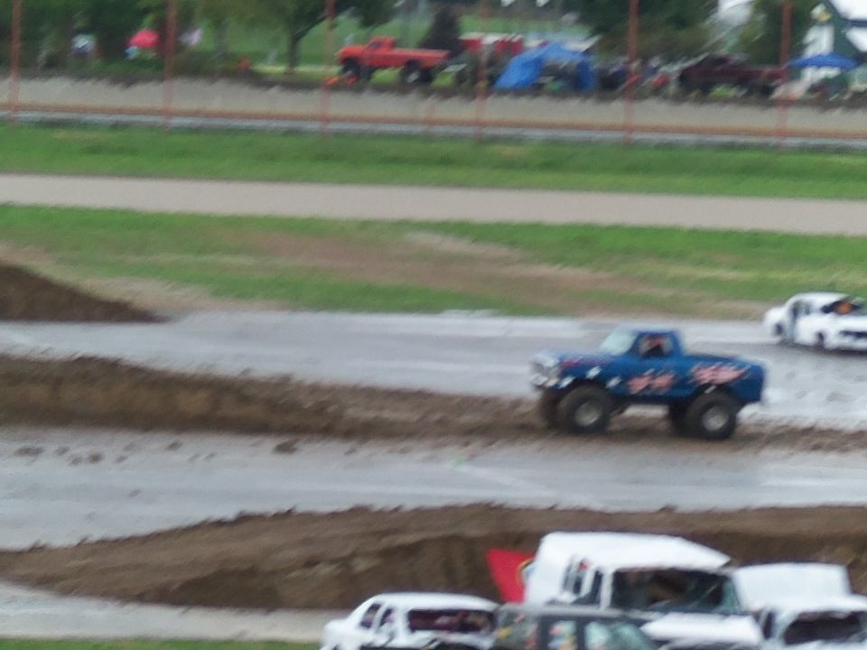 Blue monster truck with red and white graphics on side, driving on dirt track