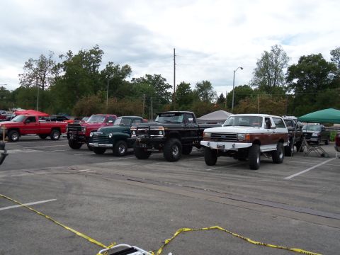 1989 Ford Bronco - Several lifted trucks and SUVs are parked in a lot, including a 1989 Ford Bronco.