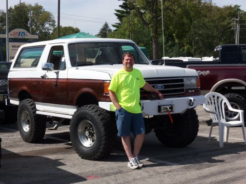 1989 Ford Bronco - A man poses next to a heavily modified white and brown 1989 Ford Bronco with large off-road tires and a custom front bumper.