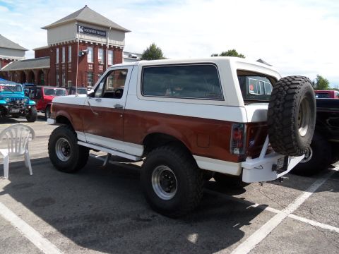 1989 Ford Bronco - This two-tone brown and white 1989 Ford Bronco features a rear-mounted spare tire and appears to be at a car show or gathering.