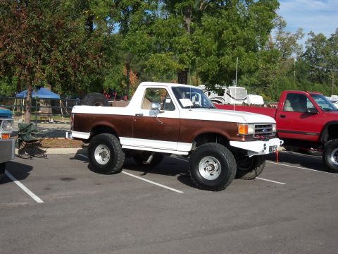 1989 Ford Bronco - A modified pickup truck with large tires and a two-tone paint job is parked in a lot.