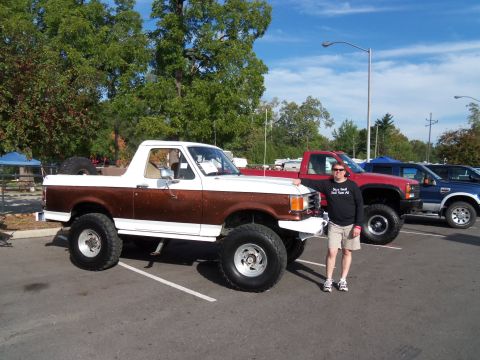 1989 Ford Bronco - A man poses with a lifted white and brown Ford Bronco, with other trucks visible in the background.