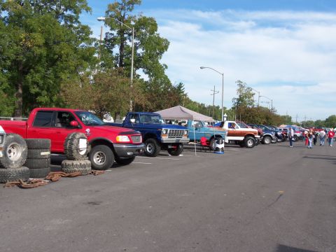 1989 Ford Bronco - A variety of trucks and SUVs are parked in a lot under a partly cloudy sky.