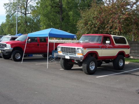 1989 Ford Bronco - A lifted red and cream Ford Bronco is parked next to a red pickup truck under a blue canopy.