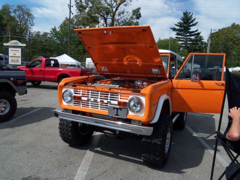 1989 Ford Bronco - An orange Ford Bronco is displayed with its hood and driver's door open, parked outdoors.