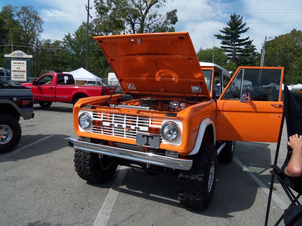 orange Ford Bronco with hood and door open, parked next to a red pickup truck