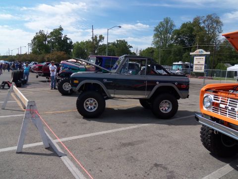 1989 Ford Bronco - A lifted gray Ford Bronco is parked in a lot with other vehicles and people.