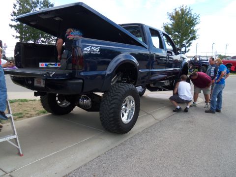 1989 Ford Bronco - A lifted pickup truck with off-road tires is examined by a group of people.