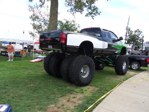 1989 Ford Bronco - A modified truck with oversized tires and a lifted suspension is parked on grass next to another truck.