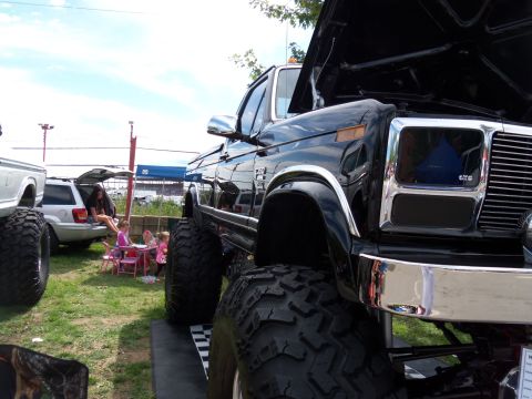 1989 Ford Bronco - A heavily modified black truck with oversized tires and a prominent chrome grille is displayed outdoors.