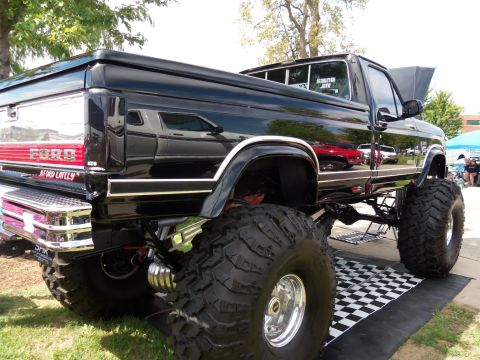 1989 Ford Bronco - This modified Ford pickup truck features oversized tires and a lifted suspension, with its hood open.