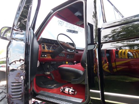 1989 Ford Bronco - The interior of a black truck features red seats, wood grain accents, and a fire extinguisher on the floor.
