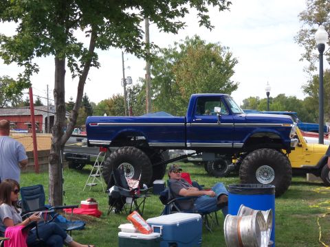 1989 Ford Bronco - A lifted blue pickup truck sits on a grassy field next to a yellow Jeep.