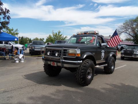 1989 Ford Bronco - Modified 1989 Ford Bronco with custom off-road tires and emergency lights is parked outdoors.
